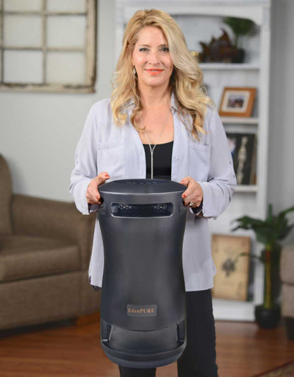 Woman holding black EdenPURE 360 Super Climater heater with curved design in living room setting